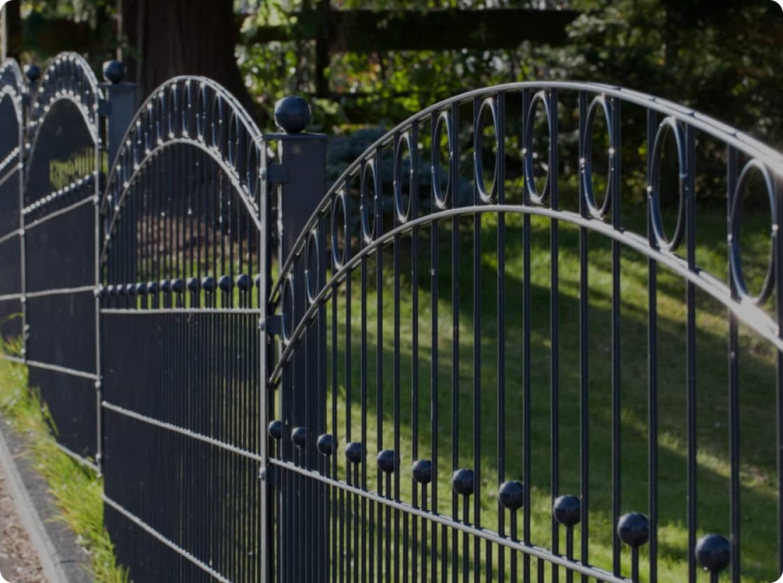 Detailaufnahme eines schwarzen Schmuckzauns mit Halbbögen in einem Garten