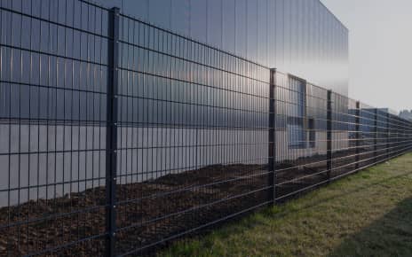 Schwarzer Gitterzaun vor einem Industriegebäude