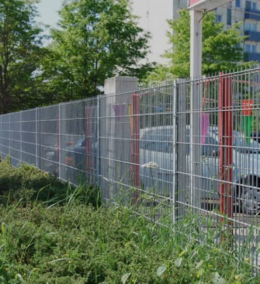 Silberner Gitterzaun vor einem Parkplatz auf Rasen