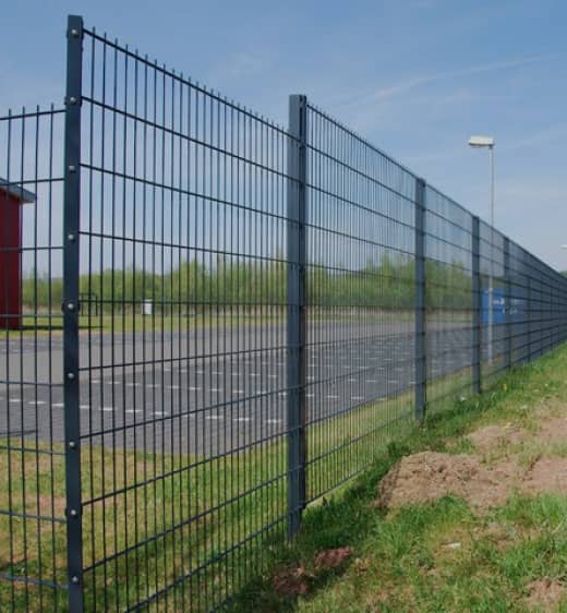 Blauer Gitterzaun vor einem Parkplatz